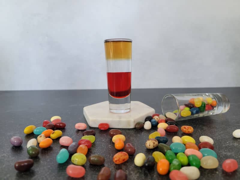 Layered Jelly Bean Shot on a white coaster surrounded by jelly bean candies